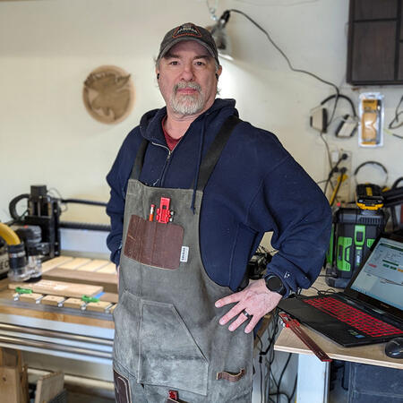 A picture of a man, wearing a canvas apron and tools in the background.